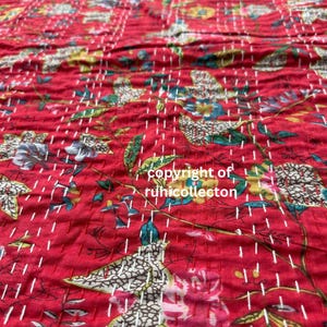 May include: Red kantha quilt with a floral pattern. The quilt is hand-stitched with white thread and has a textured surface. The quilt is made of cotton and is perfect for adding a touch of traditional Indian style to your home.