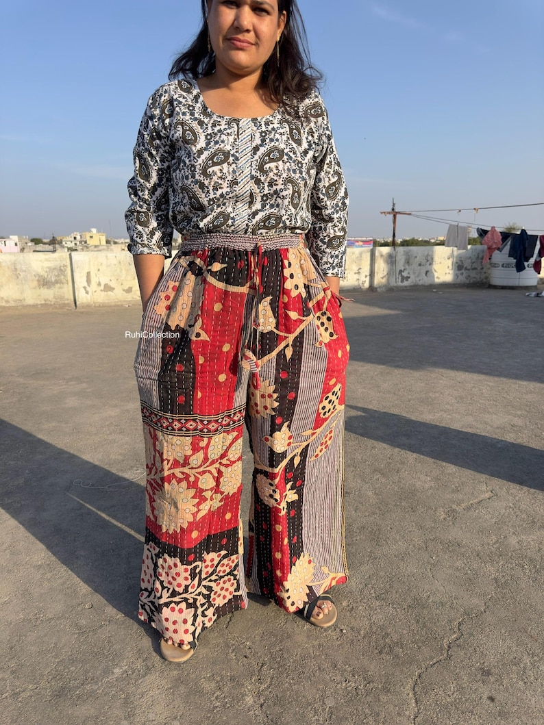 May include: A woman wearing a white and black patterned top with a red, black, and white patterned palazzo pants. The pants have a drawstring waist and a floral print.