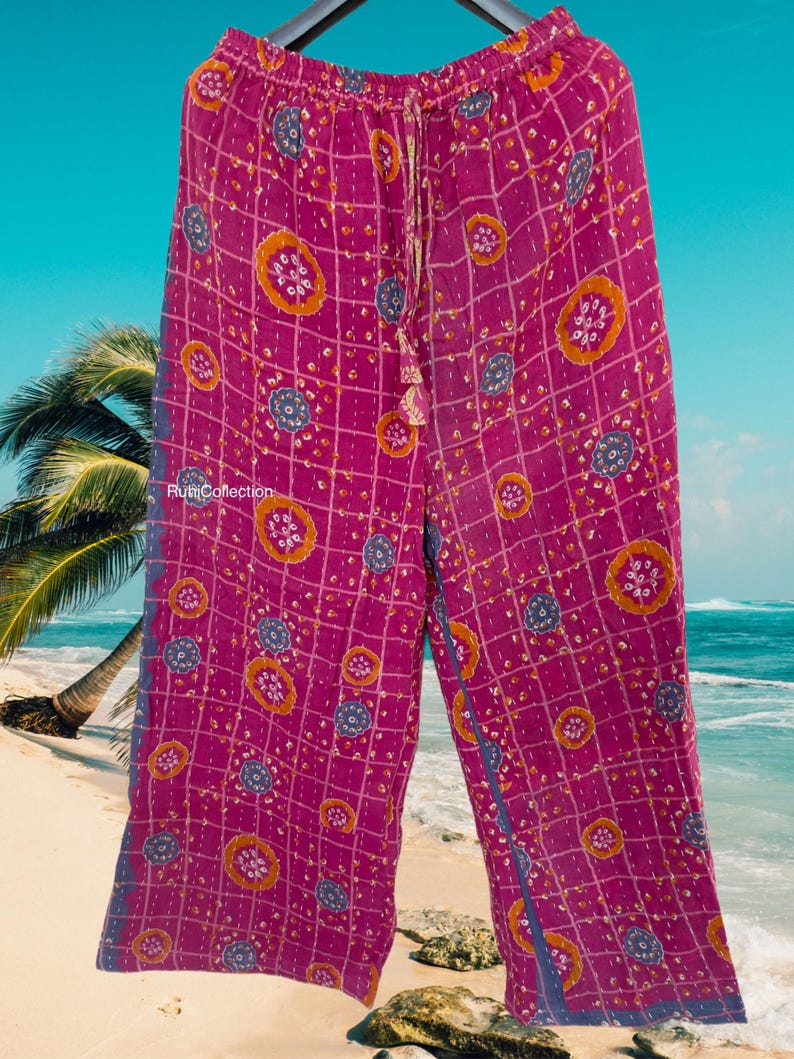 May include: Pink wide-leg pants with a geometric pattern of orange and blue circles on a grid background. The pants have a drawstring waist and a blue trim.