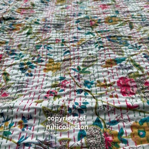 May include: White cotton fabric with a floral pattern in shades of pink, blue, green, and yellow. The fabric has a quilted texture and is decorated with small, evenly spaced lines in pink and green.