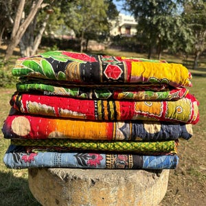 May include: A stack of colorful kantha quilts with intricate patterns and embroidery. The quilts are made of recycled saris and are perfect for adding a touch of bohemian style to any home.