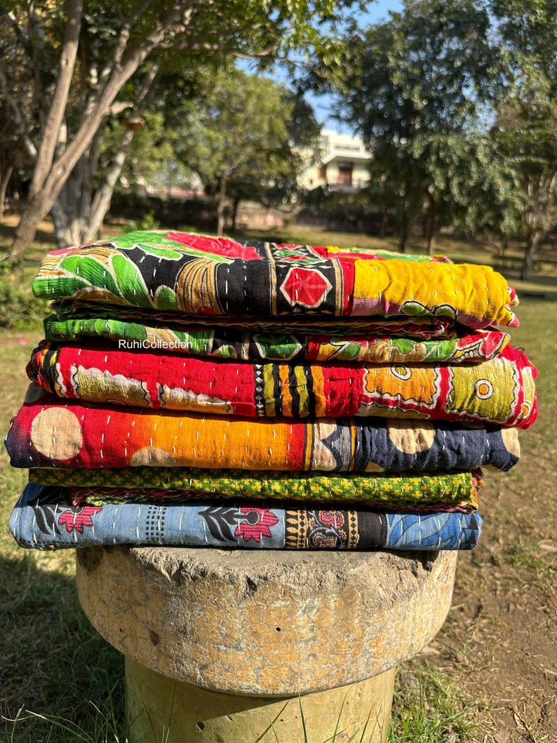 May include: A stack of colorful kantha quilts with intricate patterns and embroidery. The quilts are made of recycled saris and are perfect for adding a touch of bohemian style to any home.