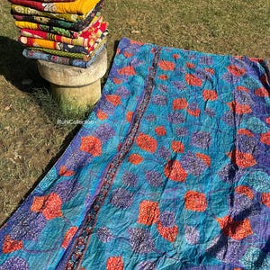 May include: A blue and purple kantha quilt with a red and white floral pattern. The quilt is made of recycled saris and is hand-stitched. It is a traditional Indian textile.
