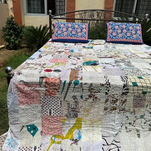 May include: A patchwork quilt and two matching pillow covers rest on a wrought iron bed frame. The quilt features a variety of fabric patterns in shades of white, pink, blue, and yellow. The pillow covers are blue with a floral design.