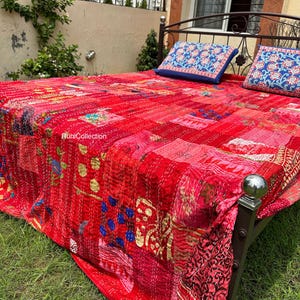 Könnte beinhalten: Eine rote Kantha-Steppdecke mit aufwendigen Stickereien und Patchwork-Details. Die Decke liegt auf einem Bett mit zwei blauen Kissen mit Blumendruck.