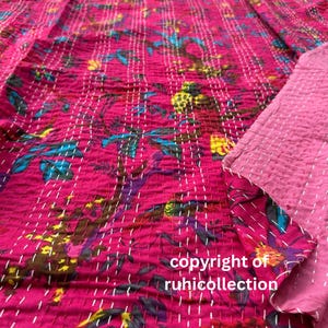 Peut inclure: Textile rose vif avec un motif floral dans les tons de bleu, vert, jaune et violet. Le tissu est cousu avec du fil blanc, et le texte "copyright of ruhicollection" est visible. Il semble s'agir d'une courtepointe ou d'une couverture.