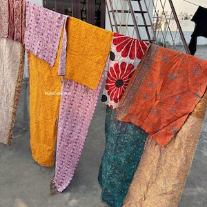 May include: A collection of six colorful kantha quilts hanging on a clothesline. The quilts are made of various fabrics, including silk, cotton, and velvet. The quilts are all different sizes and shapes, and they are all decorated with intricate embroidery. The quilts are a beautiful example of traditional Indian craftsmanship.