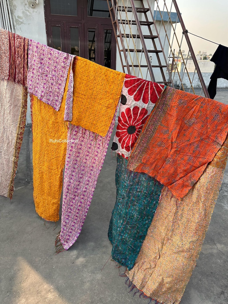 May include: A collection of six colorful kantha quilts hanging on a clothesline. The quilts are made of various fabrics, including silk, cotton, and velvet. The quilts are all different sizes and shapes, and they are all decorated with intricate embroidery. The quilts are a beautiful example of traditional Indian craftsmanship.