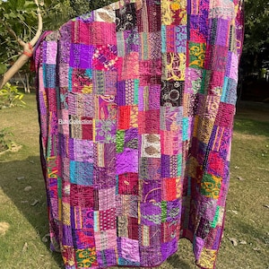May include: A patchwork quilt in shades of purple, pink, and magenta, with a variety of patterned fabric squares. The quilt is draped over a tree branch, showcasing its vibrant colors and textures. The quilt is made of various fabrics.