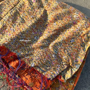 May include: A yellow, orange, and blue kantha quilt with intricate floral patterns and hand-stitched details. The quilt is folded and layered, showcasing the different colors and textures of the fabric.