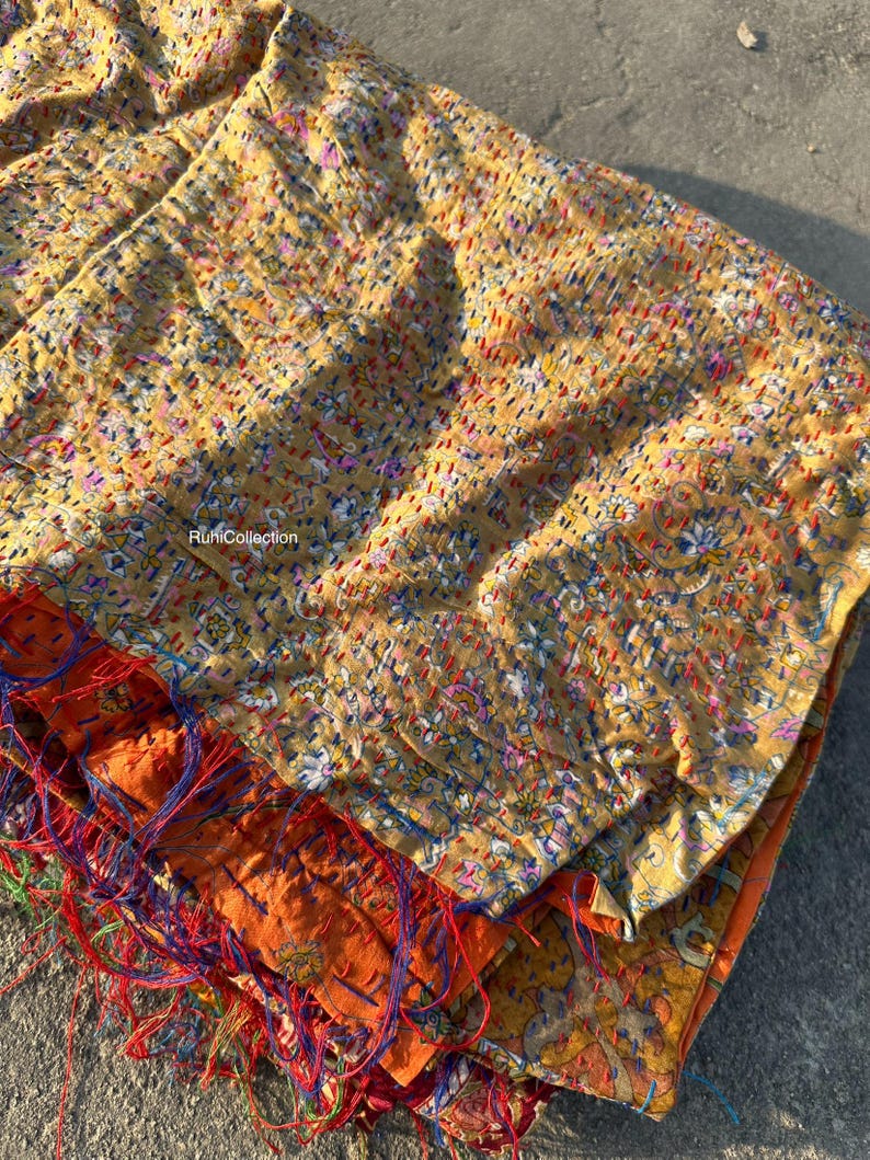 May include: A yellow, orange, and blue kantha quilt with intricate floral patterns and hand-stitched details. The quilt is folded and layered, showcasing the different colors and textures of the fabric.