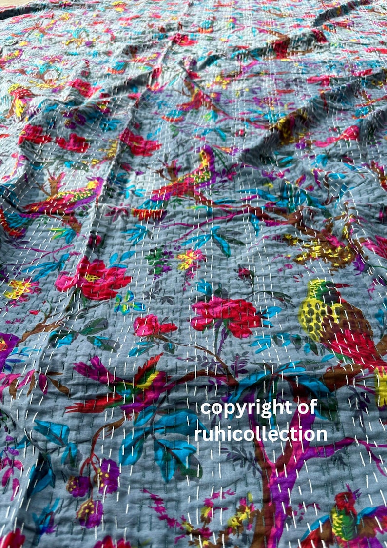 May include: A gray, quilted textile featuring a vibrant floral and bird pattern. The design includes red, pink, yellow, blue, and purple elements. The text "copyright of ruhicollection" is visible. The stitching is white.