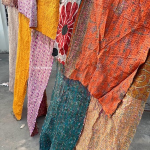 May include: A patchwork quilt made from colorful silk fabric scraps. The quilt is made up of several different patterns and colors, including orange, yellow, pink, green, and red. The quilt is hanging on a clothesline.
