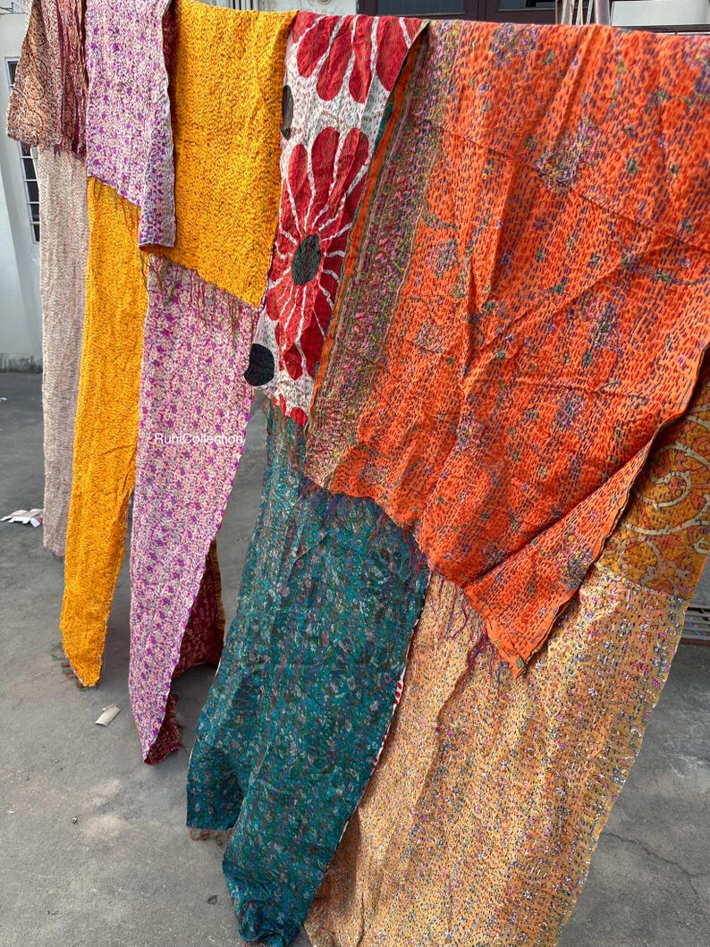 May include: A patchwork quilt made from colorful silk fabric scraps. The quilt is made up of several different patterns and colors, including orange, yellow, pink, green, and red. The quilt is hanging on a clothesline.