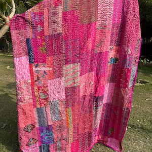Peut inclure: Une courtepointe patchwork vibrante dans les tons de rose et de magenta. La courtepointe est composée de divers carrés de tissu, chacun avec des textures et des motifs uniques. Les bords sont finis avec une bordure rose vif. Le texte "RumiCollection" est visible.