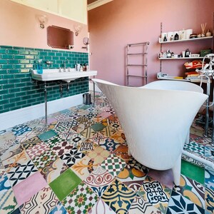 Puede incluir: Un baño lujoso con una bañera blanca con patas, un lavabo blanco y un suelo de baldosas estampadas de colores. Las paredes están pintadas de rosa y verde, con un espejo y apliques encima del lavabo. Un toallero cromado está en la pared.