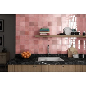 Könnte beinhalten: Eine Küchenarbeitsplatte mit einer schwarzen Marmorfläche und einem Doppelwaschbecken. Die Arbeitsplatte hat einen Holzunterbau. Die Rückwand ist mit rosa quadratischen Fliesen verkleidet. Auf der Arbeitsplatte steht eine Schüssel mit Orangen.