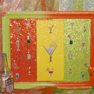 May include: A framed artwork with a glittery background depicting a variety of cocktails and liquor bottles. The frame is green and orange with a lime slice on the top right corner.