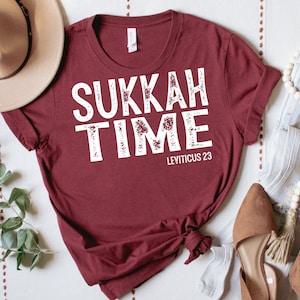 Może przedstawiać: Bordowy t-shirt z napisem "SUKKAH TIME" w kolorze białym z efektem postarzenia. Pod głównym tekstem nadrukowany jest mniejszy biały napis "LEVITICUS 23".