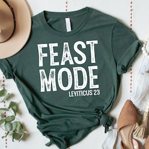 Może przedstawiać: Zielony T-shirt z napisem "FEAST MODE" w kolorze białym ze stylizowanym efektem zużycia. Pod napisem znajduje się napis "LEVITICUS 23" w mniejszej, białej czcionce.