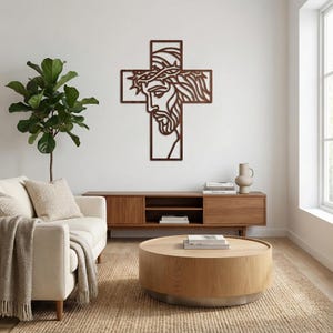 May include: A wooden cross wall art piece featuring a detailed depiction of Jesus wearing a crown of thorns. The artwork is a warm brown color and is mounted on a white wall, adding a touch of religious decor to a living space.