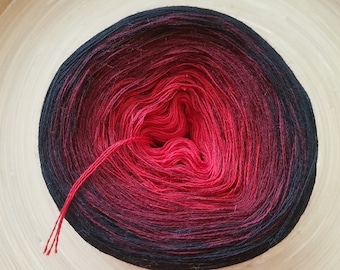 May include: A ball of yarn with a gradient of colors, transitioning from black to deep red in the center. A strand of red yarn extends from the center. The yarn is likely for knitting or crocheting.