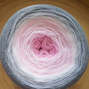 May include: A ball of yarn with a gradient effect, shifting from grey to white and then to pink at the core. The yarn is tightly wound, forming a circular shape. Ideal for knitting or crochet projects, the yarn is a soft, pastel colour.