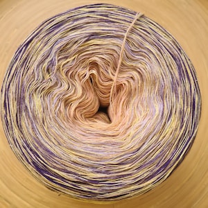 May include: A tightly wound ball of yarn with a gradient of colors. The center is a light peach color, transitioning to yellow, then purple on the outer edges. A single strand of yarn extends from the center.