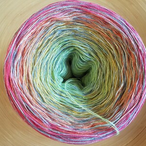 May include: A vibrant ball of yarn with a gradient of colors, including pink, orange, yellow, green, and blue. The yarn is tightly wound, creating a circular shape. The yarn is likely used for knitting or crocheting projects.