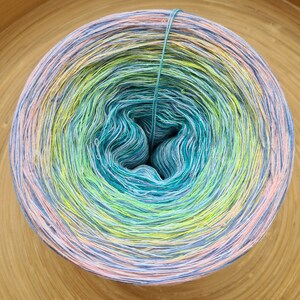 May include: A large, colorful ball of yarn with a gradient of colors, including shades of blue, green, yellow, and pink. The yarn is tightly wound, with a teal strand running through the center. The yarn is likely used for knitting or crocheting projects.