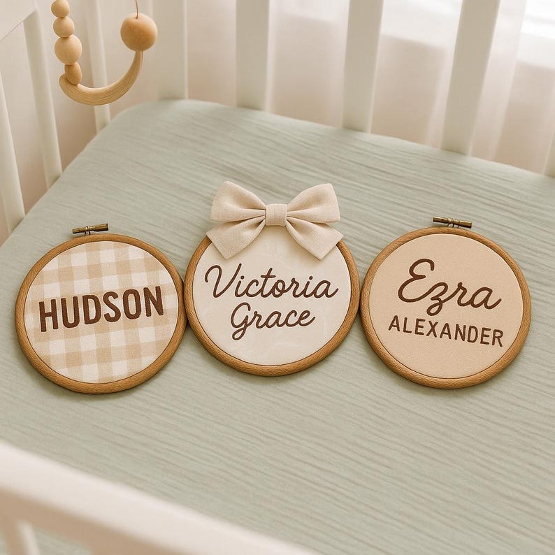 May include: Three personalized wooden name plaques. One plaque features a gingham pattern with the name "HUDSON". The second plaque has the name "Victoria Grace" and a bow. The third plaque has the name "Ezra Alexander".