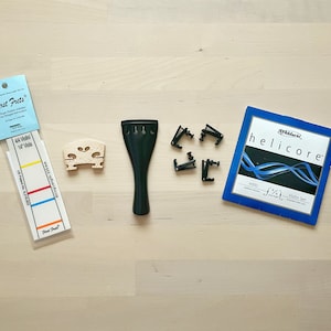 May include: A set of violin accessories including a black chin rest, a wooden bridge, a set of black fine tuners, a package of D'Addario Helicore violin strings, and a First Frets fingerboard guide.