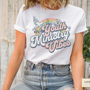 May include: White t-shirt with a rainbow and a dove graphic. The text "Youth Ministry Vibes" is in a retro font.