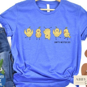May include: A blue t-shirt with a graphic of five yellow chicks with the text "Empty Nester Life".