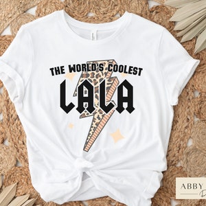 May include: White t-shirt with a graphic of a lightning bolt with a leopard print design. The text "The World's Coolest Lala" is printed on the shirt.