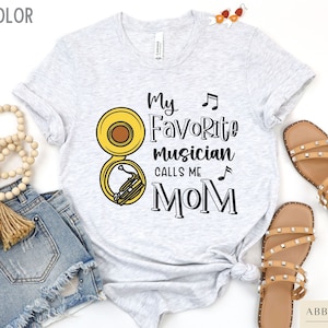 May include: A grey t-shirt with the text "My Favorite Musician Calls Me Mom" and a yellow musical instrument graphic.