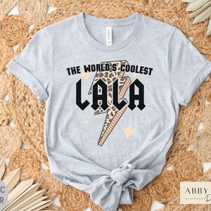 May include: A gray t-shirt with a black lightning bolt graphic and the text "The World's Coolest Lala" in black. The lightning bolt is filled with a leopard print pattern.