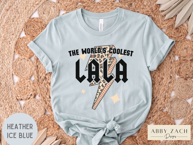 May include: A light blue t-shirt with a graphic of a lightning bolt with a leopard print design. The text "The World's Coolest Lala" is printed on the shirt.