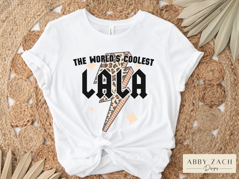 May include: White t-shirt with a graphic of a lightning bolt with a leopard print design. The text "The World's Coolest Lala" is printed on the shirt.