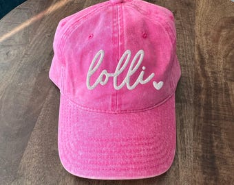 May include: Pink baseball cap with the word "olli" embroidered in white on the front.