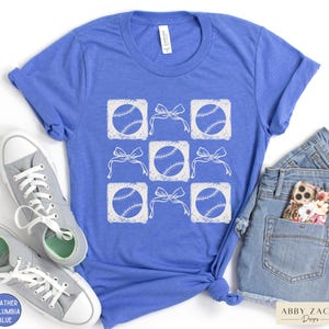 May include: A blue t-shirt with a white design of baseballs and bows. The design is in a grid pattern with each baseball in a square and a bow above it.