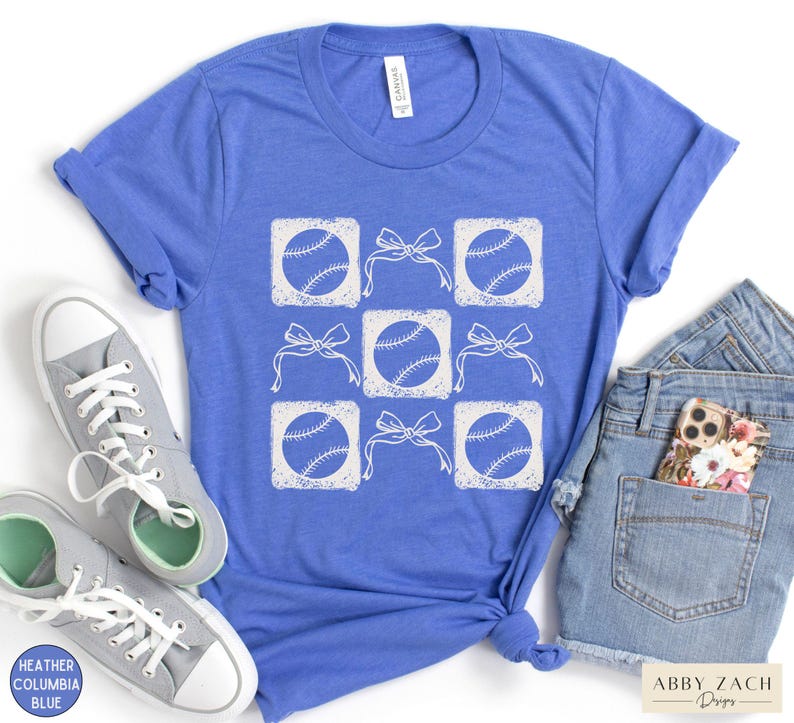 May include: A blue t-shirt with a white design of baseballs and bows. The design is in a grid pattern with each baseball in a square and a bow above it.