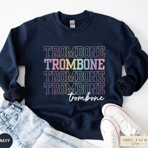 May include: Navy blue sweatshirt with the text "TROMBONE" repeated four times in rainbow colors, with a smaller "trombone" written in cursive below.