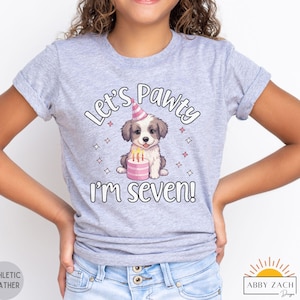May include: Gray t-shirt with a cartoon dog wearing a party hat and holding a birthday cake. The text on the shirt reads "Let's Pawty I'm Seven!"