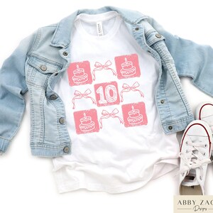 Peut inclure: T-shirt blanc avec un motif rose de cupcakes et le chiffre 10. Le motif est dispos&eacute; en grille.
