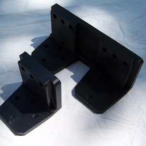 May include: Two black plastic brackets with multiple holes. The brackets are L-shaped and have a flat surface on one side.