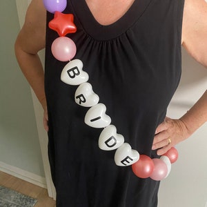 May include: A white heart-shaped balloon garland spelling "BRIDE" with pink, purple, and red balloons.