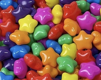 May include: A close-up of a pile of colorful star-shaped candies and oval-shaped candies. The candies are in various colors, including red, orange, yellow, green, blue, purple, and pink. The candies have a glossy finish.