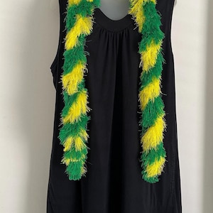 May include: A fluffy boa in alternating sections of green and yellow. The boa is draped over a black sleeveless top. The boa's texture appears soft and feathery, with a vibrant color combination. The background is a plain white wall.