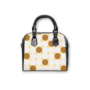 May include: A structured handbag featuring a repeating pattern of white and brown circles on a pale yellow background. The bag has black leather-like handles and black side panels, with gold-toned hardware connecting the handles to the main body.